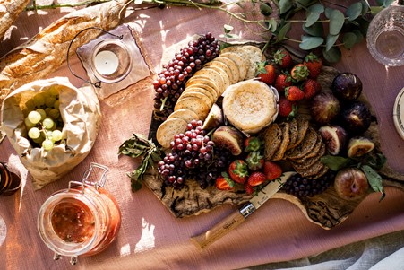Board of cheese crackers and seasonal fruit and berries on a soft pink blanket