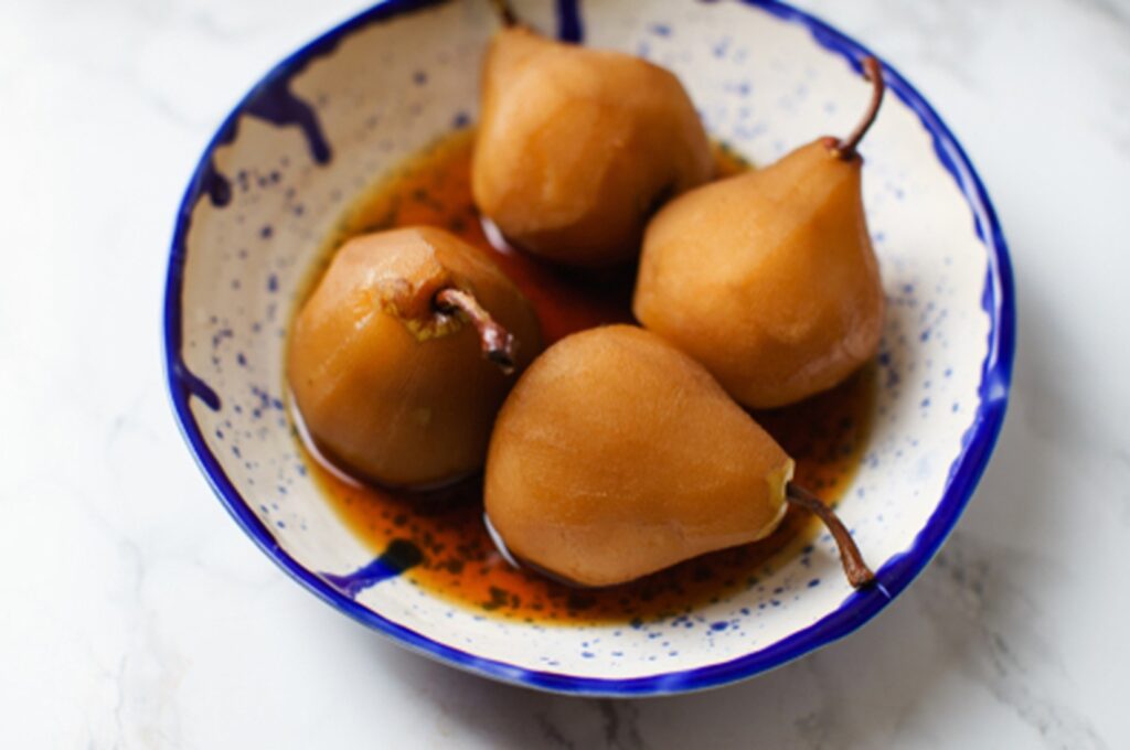 Four Poached pears in spiced tea in a ceramic blue bowl