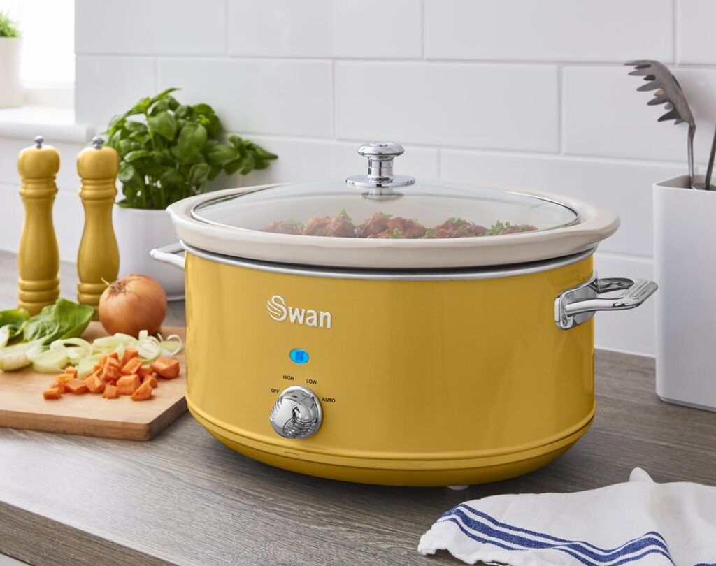 Lifestyle shot of Swans Yellow Retro Slow Cooker on a wooden countertop next to some diced onion and carrots