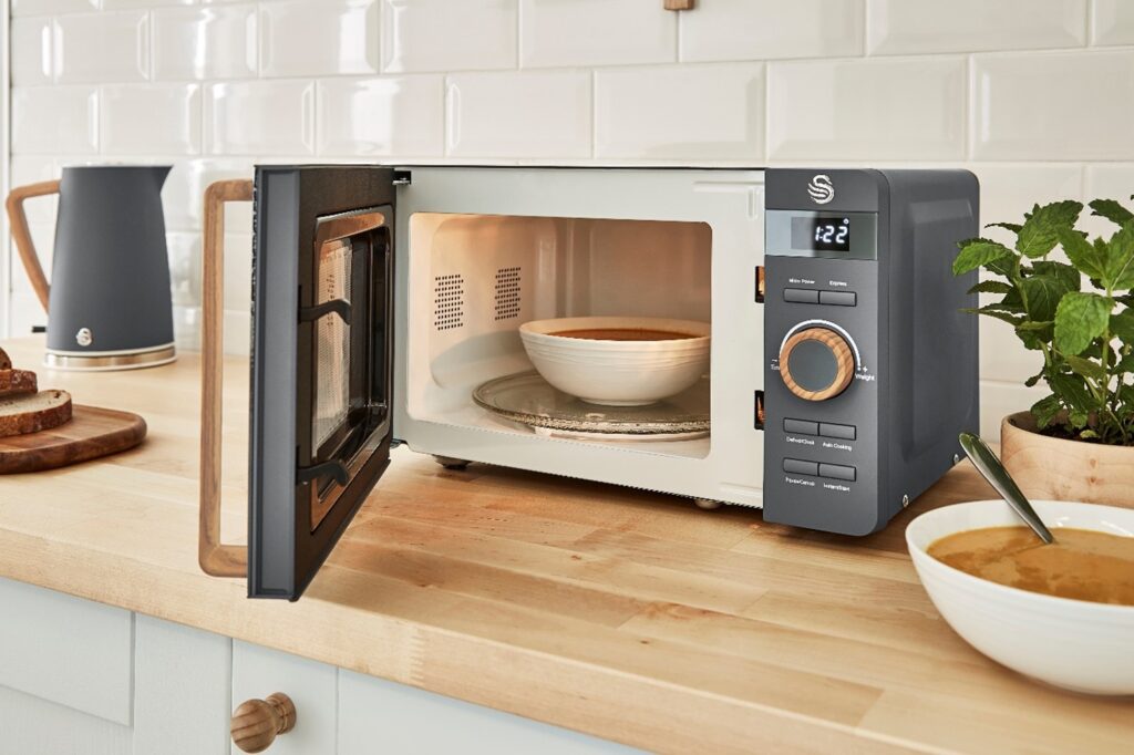 Photograph of Swan Nordic Slate Grey Microwave heating a bowl of soup next to the Swan Nordic Slate Grey Kettle