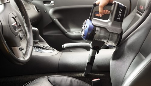 Photograph of a man using a cordless blue and black vacuum to clean the inside of his black car