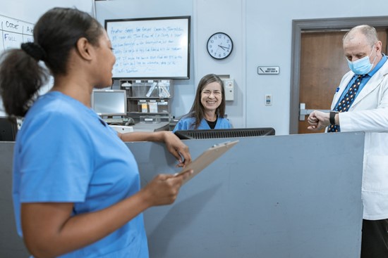 Photograph of a nurse in scrubs and a nurse at reception laughing with each other with a doctor nearby