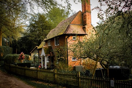Photograph of a rustic brick cottage with a front garden full of trees and flowers