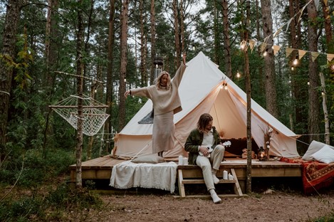 Photograph of a young couple dancing and making music in front of their white sheet tent in the woods