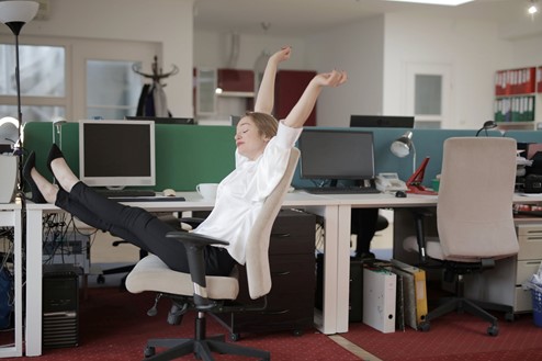 Photograph of nurse stretching in an office with her hands up in the air at her desk chair