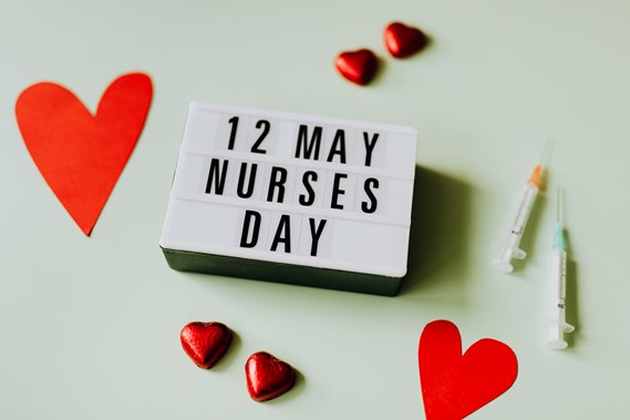 Photograph of small sign that reads 12 May Nurses Day next to cut out paper hearts heart chocolates and syringes