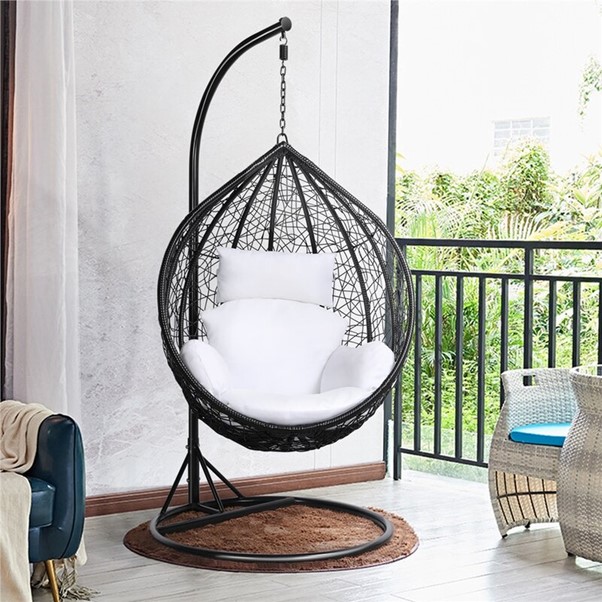 Photograph of the Argos Garden Swing Chair in an open door conservatory space next to some wicker furniture and a dark blue sofa