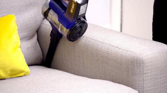 Photograph of woman using cordless hand held vacuum to clean the sides of her cream sofa