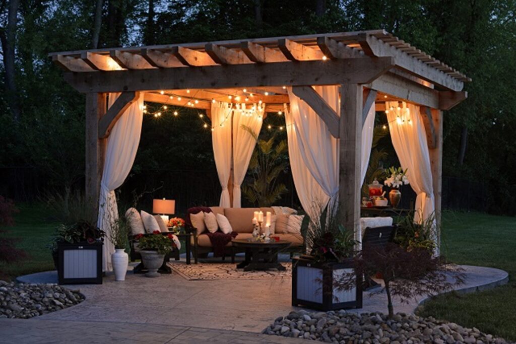 Photograph of wooden gazebo on a stone garden patio decorated with fairy lights pillows and benches