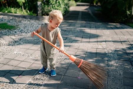 Photograph of young child cleaning a stone driveway with a wooden brush