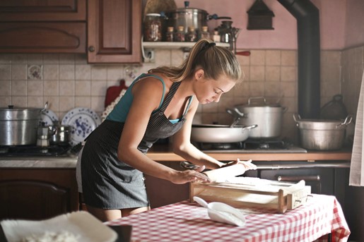 Photograph of young woman in rustic wooden kitchen rolling out her homemade pastry with a rolling pin