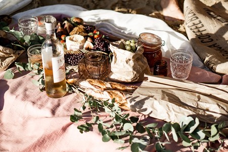 Picnic of wild berries grapes cheese and bread on a soft pink blanket