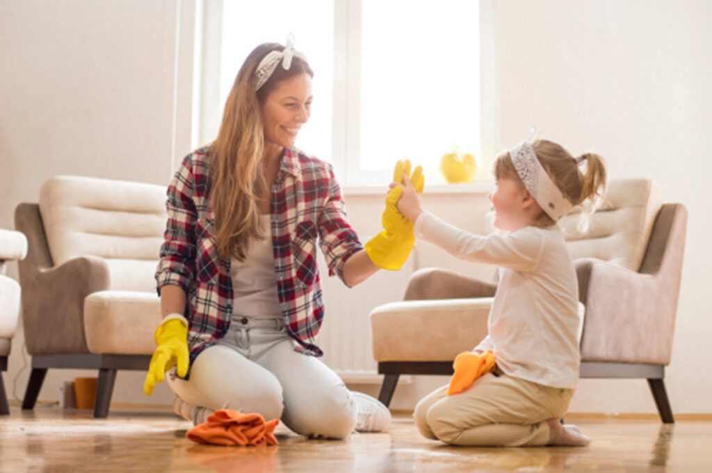 Photograph of a mother and daughter high fiving while cleaning the living room