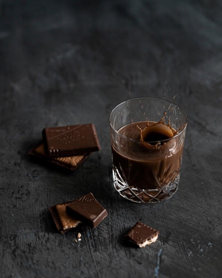 Salted Caramel Pecan Sour cocktail in small glass next to salted caramel chocolate pieces