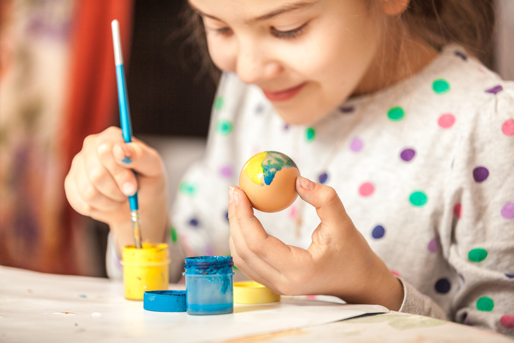 Photograph of small child painting on a egg