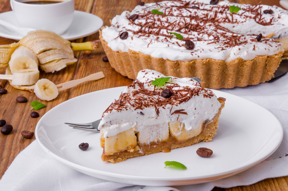 Photograph of a slice of Banoffee Pie with the full pie in the background