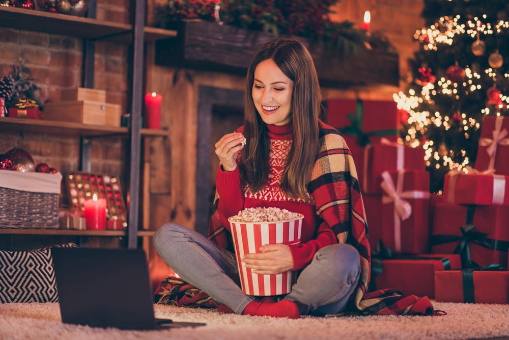 Colour image of a young woman watching Christmas films on a laptop with popcorn