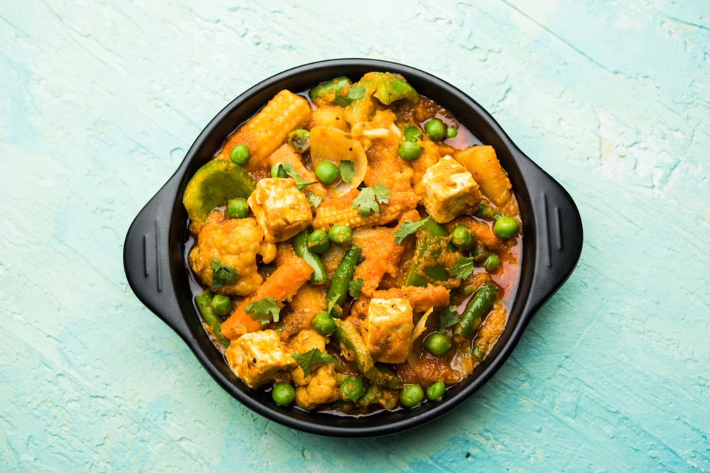 Colour image of a bowl of cauliflower curry with green beans, baby corn and peas