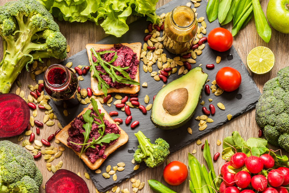 Colour image of a range of vegan foods including avocados, radish, beetroot, and hummus on toast