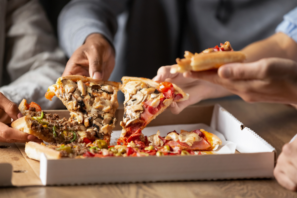 close up of people taking slices of pizza out of a takeaway pizza box