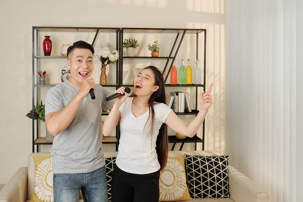 Image of a happy young couple singing karaoke into microphones in their living room