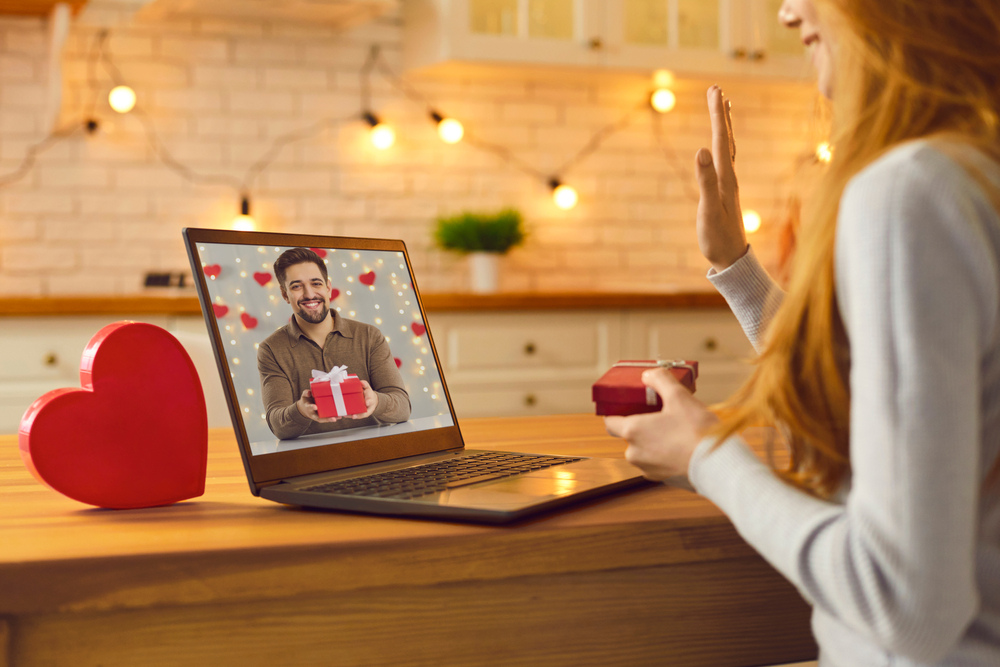 Image of a woman sat at her desk on a laptop having a valentines zoom date with her boyfriend