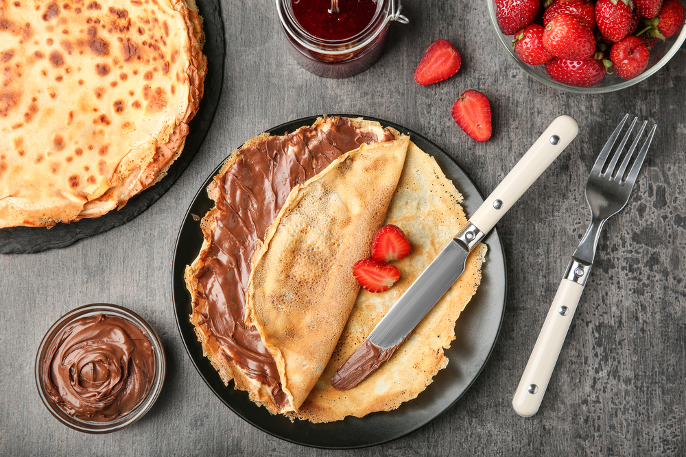 Image of a pancake on a plate with nutella spread on it and strawberries 