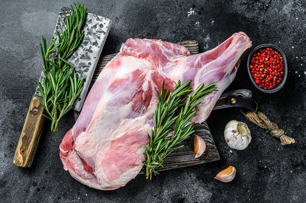 A raw lamb shoulder next to rosemary, garlic and other spices