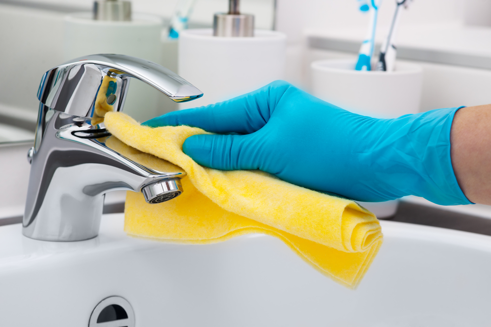 Image of a blue gloved hand cleaning a bathroom tap with a yellow cloth