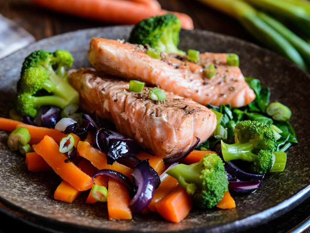 Bed of vegetables including carrots, broccoli and onions topped with two fillets of grilled salmon