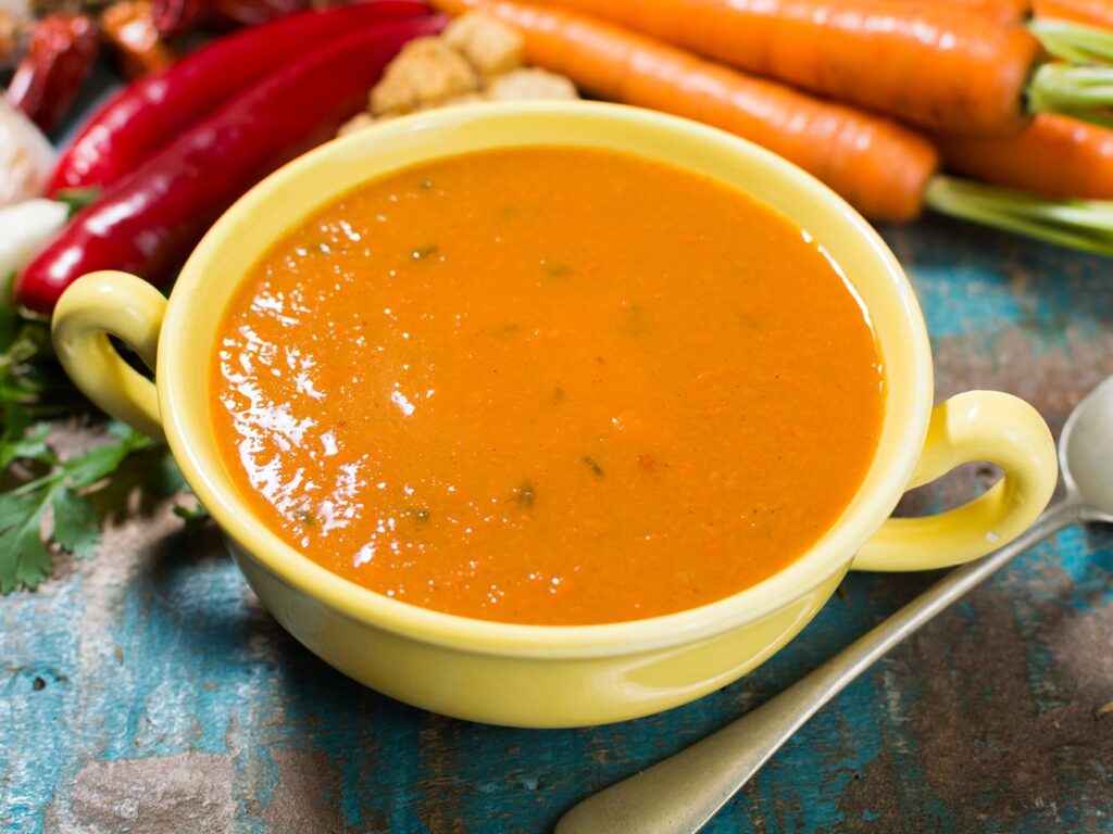 Carrot and coriander soup in a yellow bowl next to a spoon and loose carrots 
