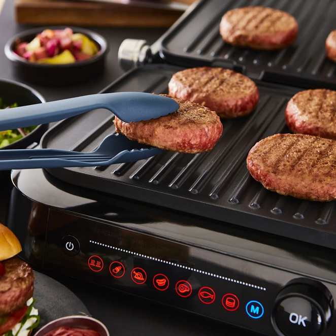 Close up of blue tongs flipping beef burgers that are cooking on the Swan Stealth Smart Grill