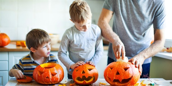 Father and his two sons carving a set of four pumpkins in their kitchen