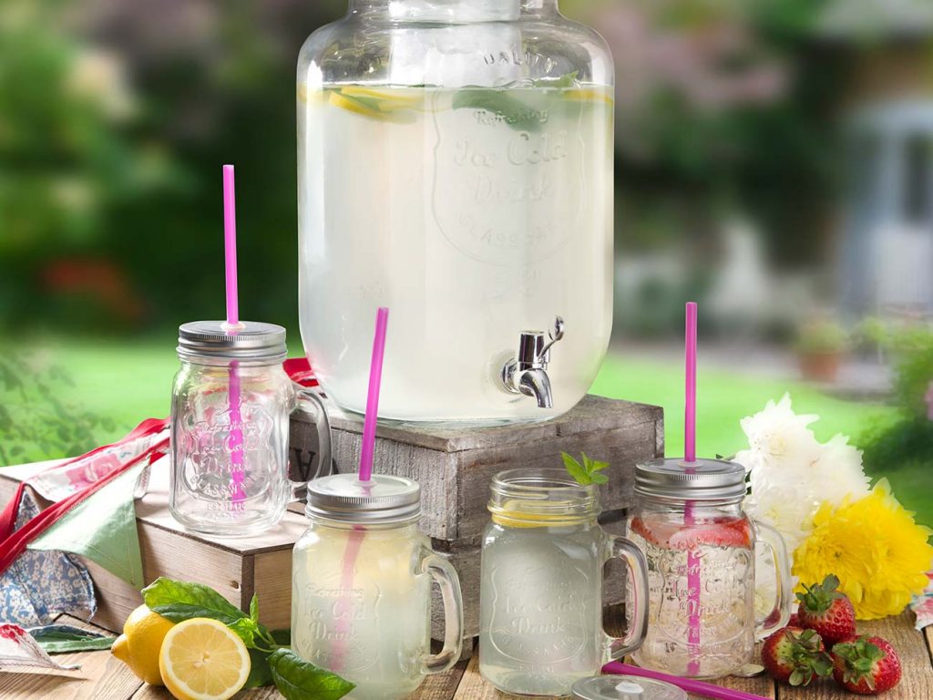 Large pitcher of cloudy lemonade on a picnic basket with small glasses full of lemonade, lemons and strawberries