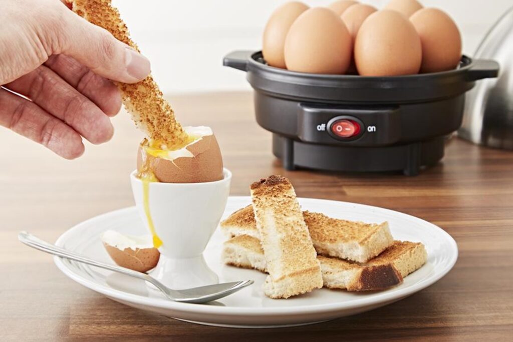 Man dipping bread soldiers into a runny boiled egg with the Swan Egg Boiler and Poacher in the background
