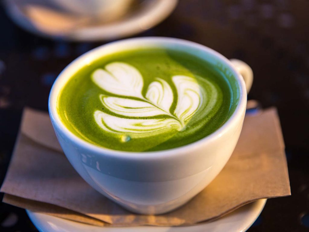 Matcha latte with leaf latte art in a white teacup resting on a white disk