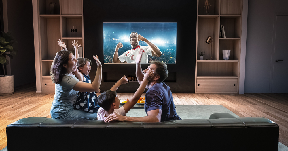 Parents and young child celebrating a football match on their sofa in front of a large TV in their living room