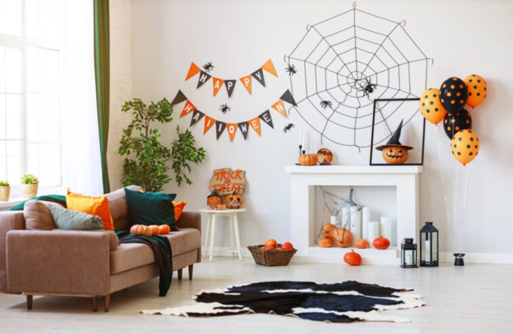 Photograph of a white living room decorated for halloween with orange and black balloons, cobwebs, plastic spiders, pumpkins and banners
