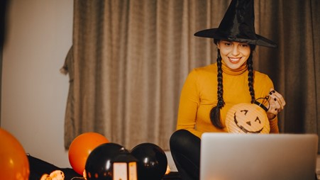 Photograph of a young woman dressed as a witch on her laptop at a virtual Halloween quarantine party