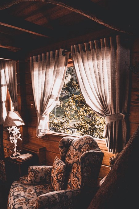 Photograph of floral armchair in a wooden cabin with beige grey curtains