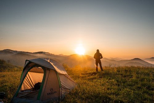 Photograph of man camping on a patch of grass overlooking mountains