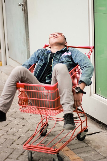 Photograph of man hungover in a small red shopping cart outside