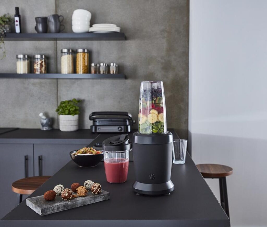 Photograph of the Swan Stealth Personal Blender in a black fitted kitchen next to a plate of trffles, a bowl of museli and fruit smoothie