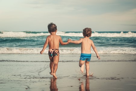 Photograph of two young children holding hands and playing at the beach