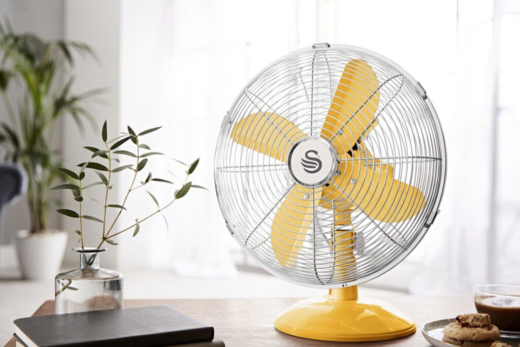 Retro yellow desk fan on a wooden desk with potted plants