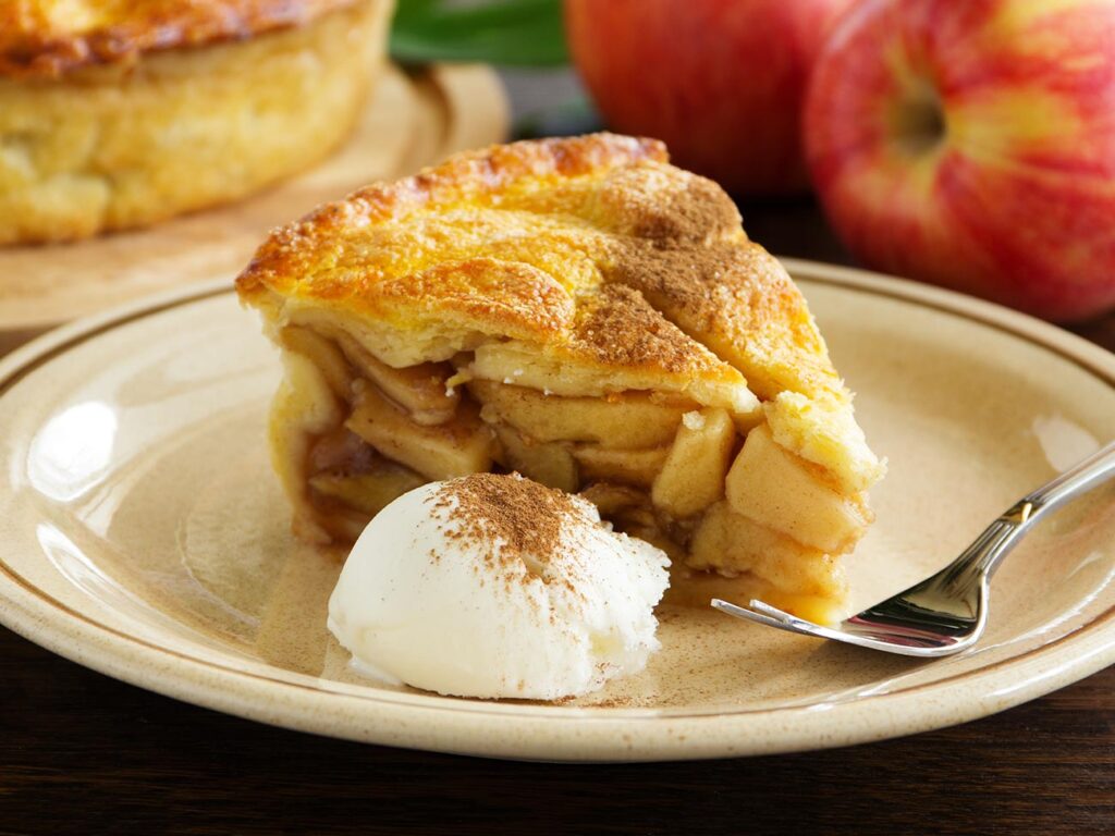 Slice of apple pie with a pile of clotted cream on a white plate