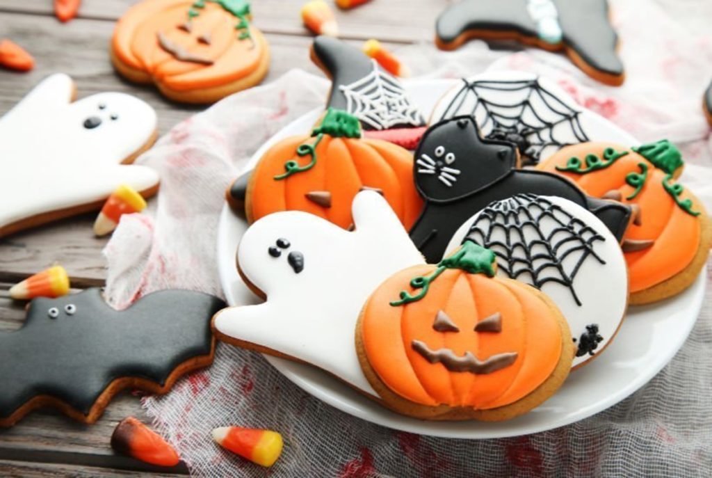 Small white plate full of Halloween decorated biscuits such as a pumpkin, ghost, cobwebs and a black cat