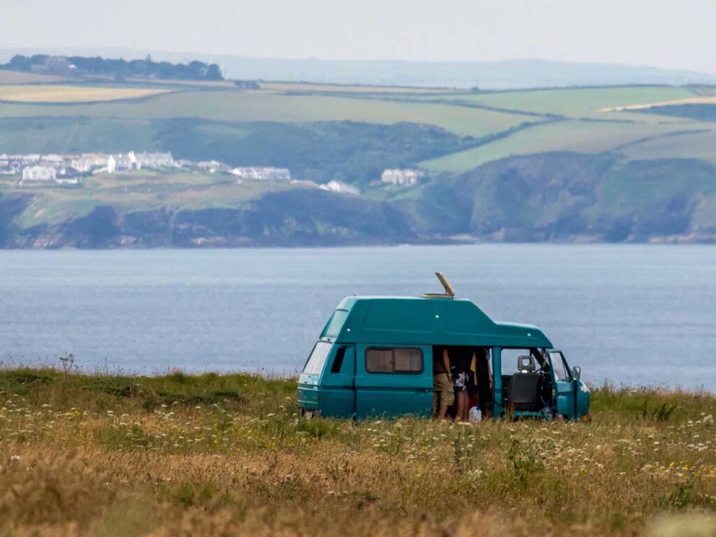 Teal blue caravan parked on a grass hill overlooking an ocean and cliffs