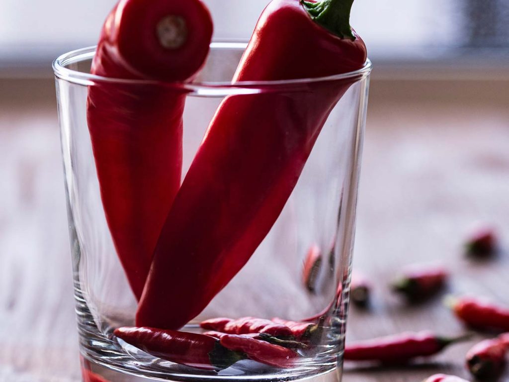 Two red chillies in a small clear glass on a wooden table