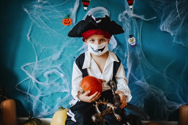 Young child dressed as a pirate wearing a COVID surgical mask decorated into a face for Halloween